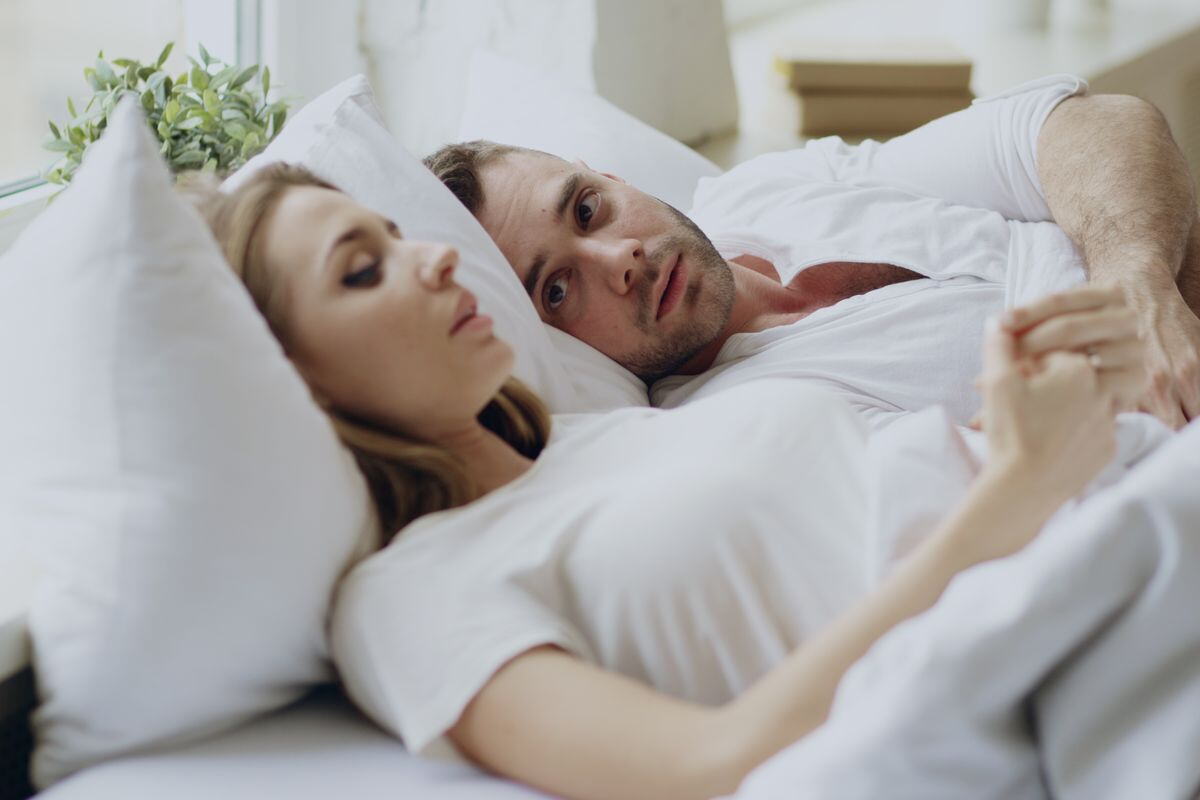 A couple lying in bed, she is lost in thought while he looks at her, before she tells him what is on her mind