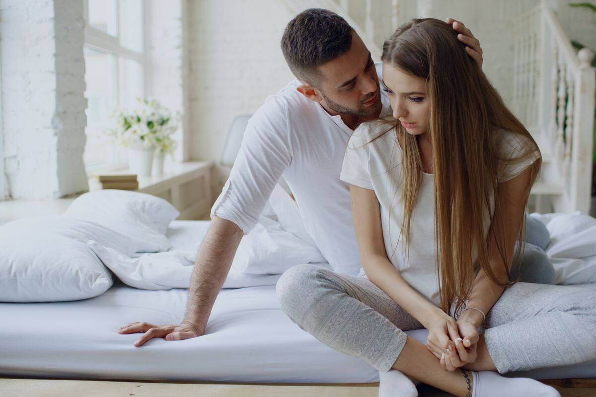 A man sitting close to his partner on the bed and comforting her as she works through her worries