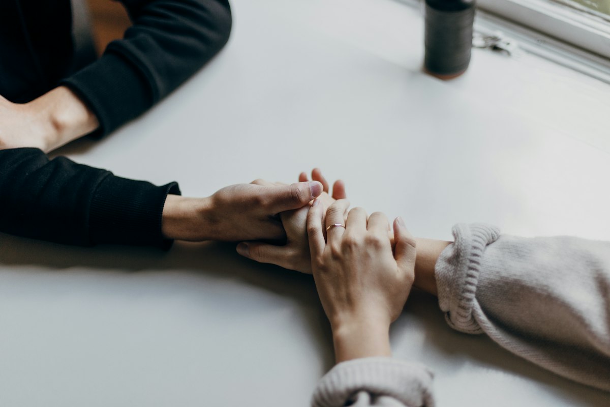 Two people holding hands across a white table as one reassures the other